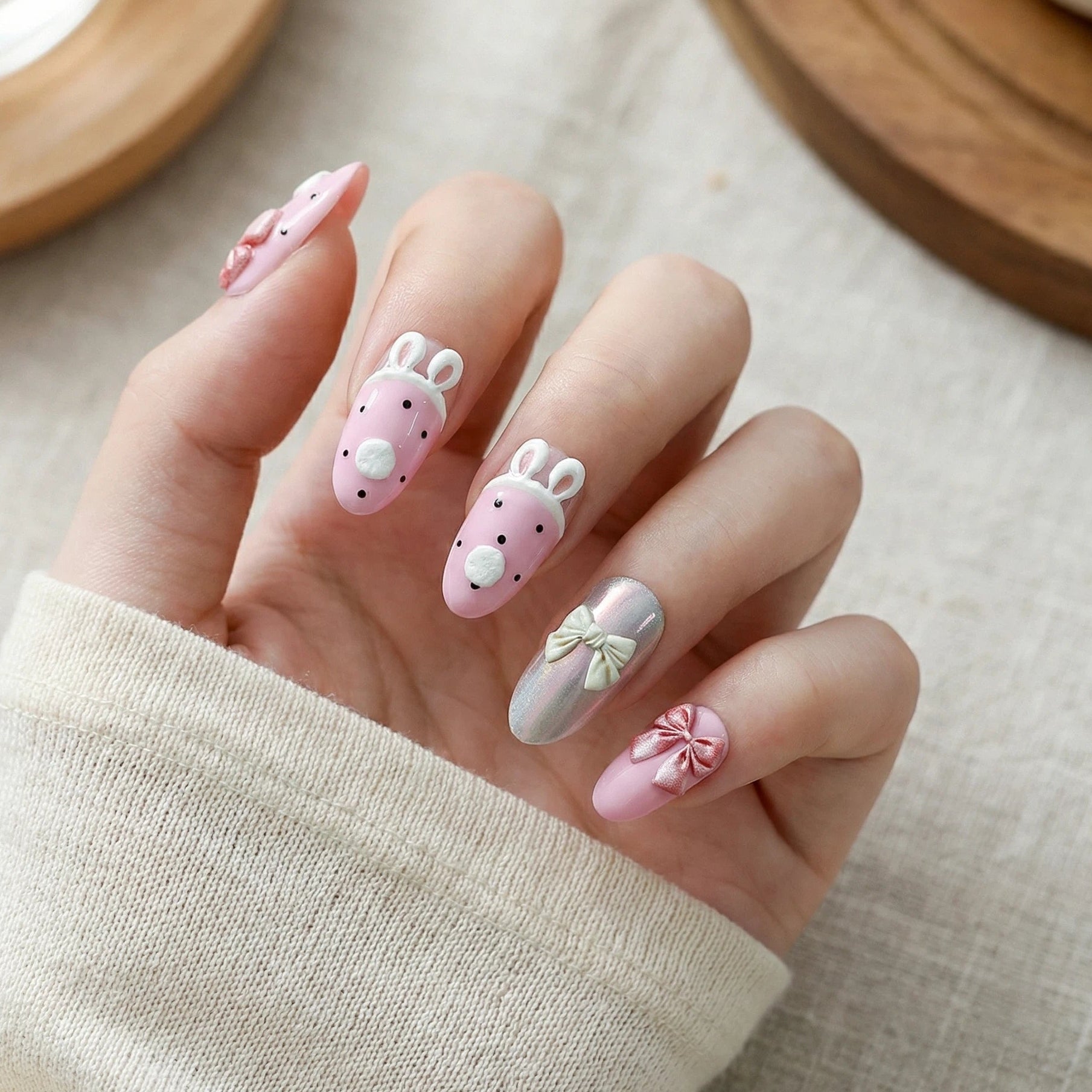 Adorable 3D bunny nail art with a pink base, paired with 3D bowknots and an aurora-effect accent nail, presented against an off-white knit sweater background.