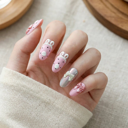 Adorable 3D bunny nail art with a pink base, paired with 3D bowknots and an aurora-effect accent nail, presented against an off-white knit sweater background.